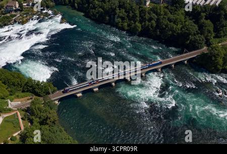 Aus der Vogelperspektive eines Zuges, der über eine Brücke über den aufgewühlten, türkisfarbenen Rhein überquert, mit den mächtigen Rheinfällen in der Nähe, Filisur, Schweiz Stockfoto