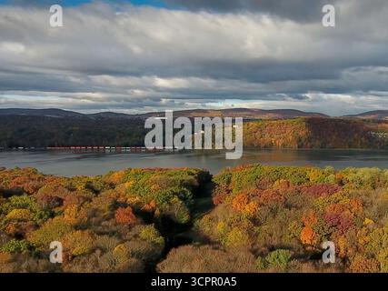 Blick aus der Vogelperspektive auf einen Fluss, der durch Wälder fließt und in Herbsttönen gemalt ist, mit einer Brücke, die anmutig über dem Wasser verläuft, Hudson River Stockfoto