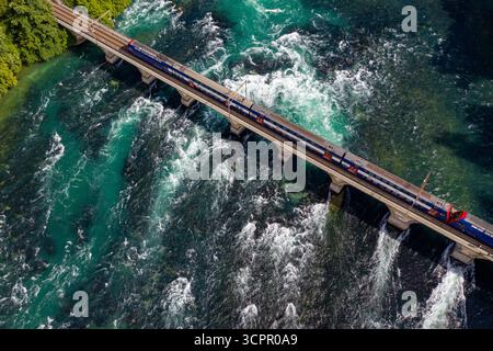 Aus der Vogelperspektive eines Zuges, der eine Steinbrücke über das türkisfarbene Wasser eines schnellen Flusses überquert, im Kontrast zu den dunklen Tiefen darunter, Schaffau Stockfoto