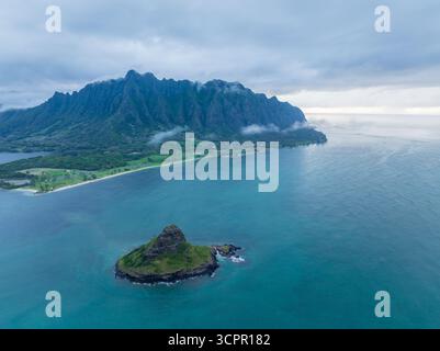 Aus der Vogelperspektive auf die grüne Chinaman's hat Island und die majestätische Ko'olau Bergkette treffen auf das türkisfarbene Meer unter einem bewölkten Himmel, Honolulu, Hawaii, USA. Stockfoto