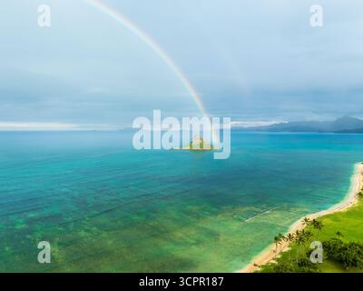 Aus der Vogelperspektive auf die pulsierende grüne Küste und die berühmte Chinaman's hat Insel unter einem leuchtenden Regenbogen, Honolulu, Hawaii, USA. Stockfoto