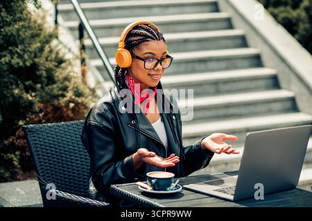 Junge, stilvolle Frau, die an einem sonnigen Morgen in der Stadt Freizeit mit Laptop und Kopfhörern genießt Stockfoto