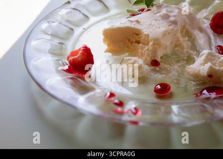 Nahaufnahme von Vanilleeis mit Schlagsahne, frischen Himbeeren und roten Siruptropfen auf einer Glasplatte. Süßes Dessert, Sommervergnügen und köstlich Stockfoto