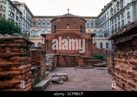 Die alte Rotunde des Heiligen Georg in Sofia, Bulgarien, eine frühchristliche Kirche aus rotem Backstein, umgeben von römischen Ruinen und modernen Gebäuden. Stockfoto
