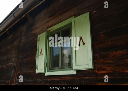 Nahaufnahme eines grünen Holzfensters mit ausgeschnittenen Motiven auf einem rustikalen Haus in Drvengrad, Serbien. Stockfoto