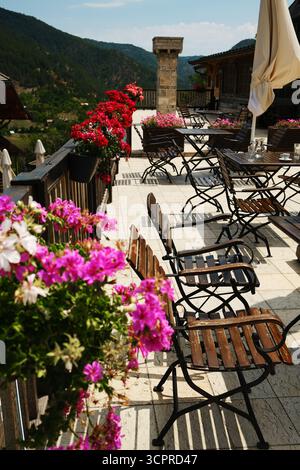 Sitzgelegenheiten im Freien mit Holztischen und Blumen auf der Terrasse in Drvengrad, Mokra Gora, Serbien. Stockfoto