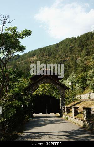 Steineingangstor mit einem Holzkreuz in Mokra Gora, das zu einem Klosterkomplex führt. Serbien Land. Stockfoto