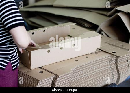 Eine Frau faltet eine Schachtel Wellpappe. Kartons für die Lieferung Stockfoto