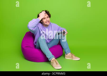 Junger Mann, der Videospiele vor grünem Hintergrund spielt, lässiges Outfit und intensiver Ausdruck, der den Controller hält Stockfoto