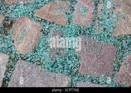 Kleine Würfel aus zersplittertem Sicherheitsglas liegen wie eine glitzernde Schicht über Pflastersteinen verstreut. Die dicken Bruchstücke deuten auf ein kaputtes Autofenster hin Stockfoto