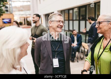 Glücklicher Geschäftsmann im Gespräch mit Unternehmerinnen bei einer Networking-Veranstaltung im Kongresszentrum Stockfoto