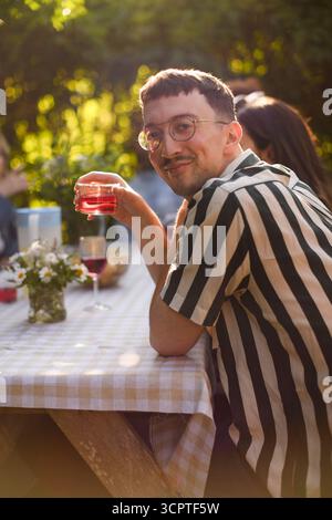 Porträt eines lächelnden jungen Mannes, der ein Glas Wein hält, während er am Tisch für eine Dinnerparty sitzt Stockfoto