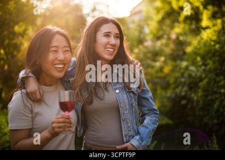 Glückliche junge Frau, die Weinglas hält, mit Arm um eine Freundin Stockfoto