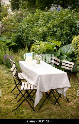 Esstisch bedeckt mit Tischdecke in der Nähe leerer Stühle im Hinterhof Stockfoto