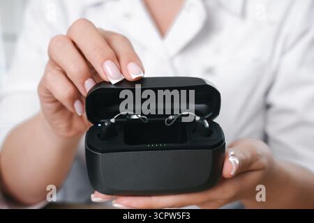 Arzthände halten eine offene Ladetasche mit zwei digitalen Hörgeräten. Moderne Assistivtechnik für Hörgesundheit und täglichen Gebrauch Stockfoto