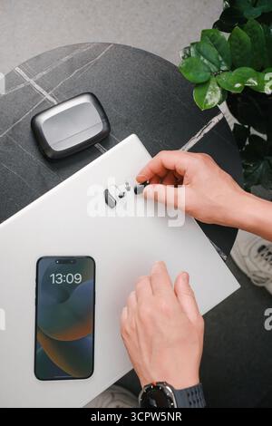 Moderne digitale Hörgeräte mit Ladetasche auf schwarzem Marmortisch, Brille, Smartphone und Notebook. Täglicher Zugang für Profis Stockfoto