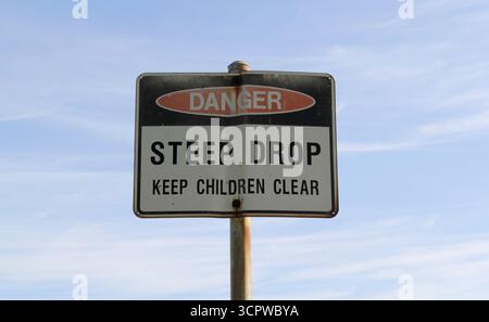 „Gefahr. Steiler Abstieg. Halten Sie Kinder klar. Warnschild mit blauem Himmel und Wolken im Hintergrund Stockfoto