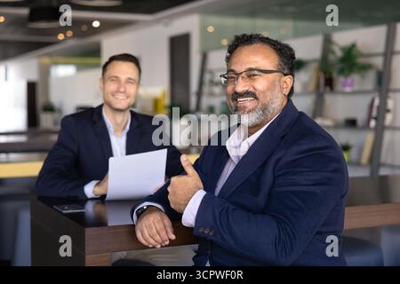 Ein glücklicher, alter indischer Geschäftsmann, der vor der Kamera eine Geste zeigt Stockfoto