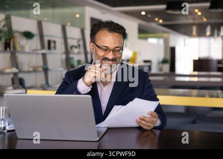 Lächelnder indischer Geschäftsmann im Jackett, der Dokumente überprüft Stockfoto
