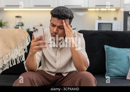 Der indische Mann zu Hause spielt die mobile Spielrunde verliert die Facepalm verärgert und ist bereit für das Rückspiel. Arabian Guy auf Sofa Tips versuchen Sie es erneut auf Smartphone Pläne Comeback konzentriert sich auf die nächste Stufe und die Wiederherstellung der Punktzahl Stockfoto