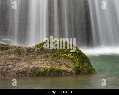 Nahaufnahme von Waterfall Cascading Down Rocks – vertikale Aufnahme mit Langzeitbelichtung, um einen seidenweichen, glatten Effekt von Wasser zu erzeugen, das über strukturierte, rote Flecken strömt Stockfoto
