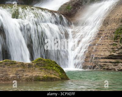 Nahaufnahme von Waterfall Cascading Down Rocks – vertikale Aufnahme mit Langzeitbelichtung, um einen seidenweichen, glatten Effekt von Wasser zu erzeugen, das über strukturierte, rote Flecken strömt Stockfoto