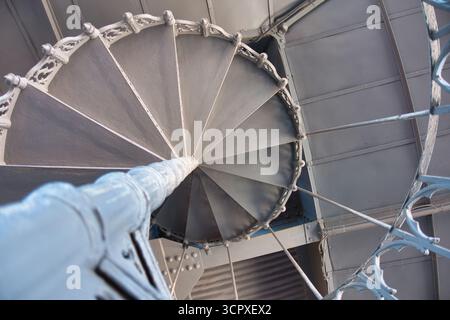 Abstrakte Eisenspiraltreppe mit Blick nach oben - dramatischer Blick aus dem niedrigen Winkel direkt nach oben eine graue, kunstvoll verzierte, schmiedeeiserne Wendeltreppe im Inneren des Histors Stockfoto