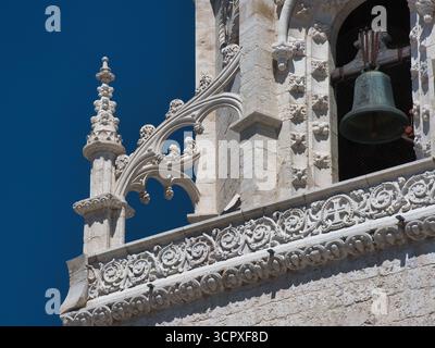 Bell Tower Detail und Blue Sky, Lissabon - komplizierte Steinschnitzereien und eine alte Bronzeglocke vor einem leuchtend blauen Himmel auf einem historischen katholischen chur Stockfoto