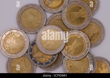 Nahaufnahme verstreuter 2-Euro-Münzen auf hellgrauer Oberfläche, die verschiedene nationale Designs und die gemeinsame europäische Seite zeigen. Stockfoto