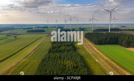 Panoramablick auf Windturbinen in einer ländlichen Landschaft mit landwirtschaftlichen Feldern, grünen Baumgruppen und teilweise bewölktem Himmel. Stockfoto