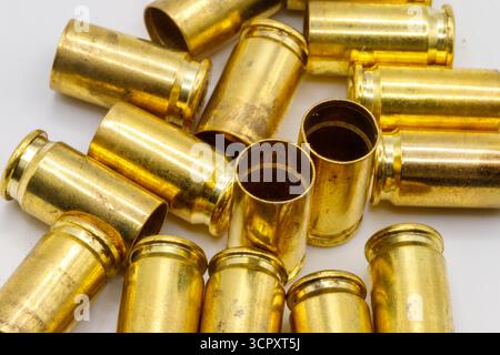 Eine Sammlung verbrauchter Messinggehäuse ist über eine weiße Oberfläche verstreut. Das goldene Metall reflektiert das Licht und hebt seine zylindrischen Formen hervor Stockfoto