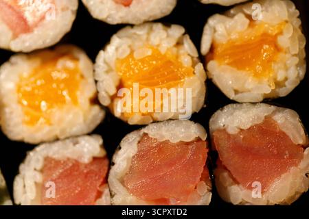 Nahaufnahme einer Makroaufnahme mit verschiedenen Sushi-Brötchen mit Lachs- und Thunfischfüllungen vor dunklem Hintergrund. Stockfoto
