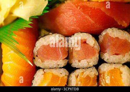 Eine Nahaufnahme mit verschiedenen Sushi-Brötchen und Sashimi. Leuchtender orangener Lachs, rosafarbener Thunfisch und blassgelber eingelegter Ingwer sind sichtbar. Stockfoto