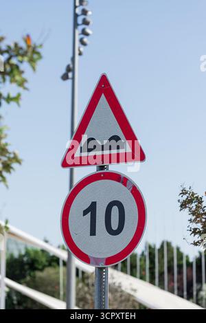 Zwei Verkehrsschilder, ein dreieckiges Warnschild vor Unebenheiten und eine kreisförmige Geschwindigkeitsbegrenzung von 10, sind an einem Metallpfosten gegen einen klaren blauen Himmel angebracht. Stockfoto