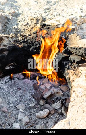 Flammen brennen in einer felsigen Grube mit dunkler, aschiger Umgebung und hellen Felsformationen. Stockfoto