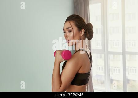 Eine junge Frau, die Hanteltraining macht, an der Armstärke arbeitet, sich den Kopierraum anschaut. Lächelnde Athletikerin, die Kurzhanteln hebt Stockfoto