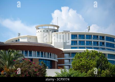 Außenaufnahme eines mehrstöckigen Gebäudekomplexes mit abgerundeten architektonischen Elementen, blauen Fenstern und umgebendem Grün unter blauem Himmel. Stockfoto