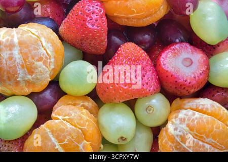 Obstsalat Mischung mit Erdbeeren, Trauben und geschälten Mandarinen flach gelegt voller Rahmen Hintergrund. Stockfoto