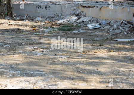Bild eines mit Schutt übersäten Bodens vor einer teilweise zerstörten Betonkonstruktion, beleuchtet durch Sonnenlicht und verstreute Schatten. Stockfoto