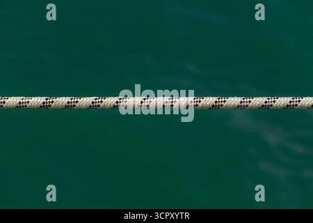 Ein weißes und schwarzes Seil erstreckt sich horizontal über das Bild vor einem unscharfen dunkelgrünen Hintergrund. Stockfoto