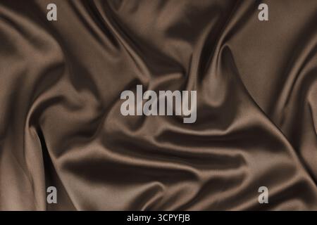 Zerknitterte, zerknitterte braune, glänzende Seidensatin-Textur. Glänzender glatter Stoff mit weichen Falten, Stoff mit Wellenvorhang. Eleganter und satter Hintergrund, Stockfoto