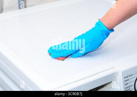 Weibliche Hand in Gummihandschuh Waschmaschine mit Schwamm Stockfoto