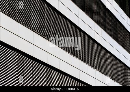 Moderne architektonische Fassade mit horizontalen Metallschlitzen und reflektierenden Paneelen für klaren geometrischen Rhythmus und Symmetrie Stockfoto