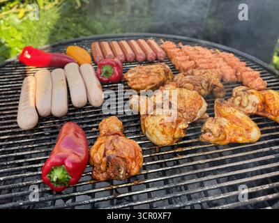 Grill mit Hühnerfleisch, Würstchen und Gemüse, das draußen mit Rauch zubereitet wird Stockfoto