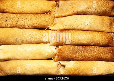 Gebratene und gerollte Pfannkuchen nebeneinander auf einer dunklen Oberfläche, Ansicht von oben, Nahaufnahme Stockfoto