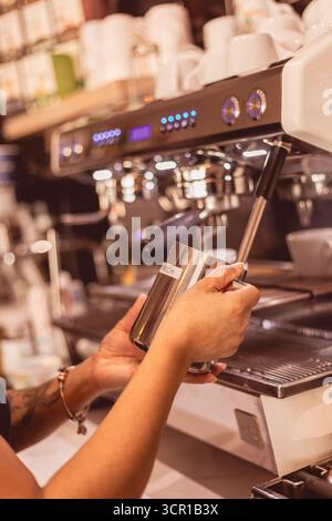Ein erfahrener Barista zieht gekonnt einen Espresso-Shot mit einer Espressomaschine. Der Laden ist lebhaft und Kaffeeliebhaber genießen ihre Getränke. Stockfoto