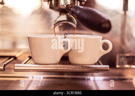 Aus einer glänzenden Espressomaschine in einem belebten Café fließt Kaffee in zwei weiße Espressomaschinen und fängt die lebendige Morgenenergie und das Aroma von Fre ein Stockfoto