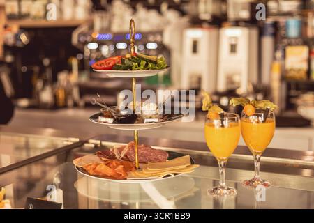 Eine zweistufige Platte mit leckerem Fleisch, Käse und frischem Gemüse ergänzt die Getränke in einem lebhaften Café während der Brunch-Stunden, cre Stockfoto