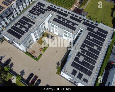 Blick aus der Vogelperspektive auf ein modernes Gebäude mit einem Dach mit Solarpaneelen. In der Umgebung gibt es Grünflächen und Parkplätze. Die Szene ist Stockfoto