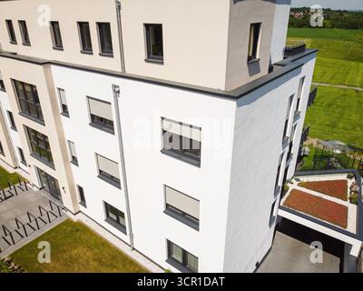 Dieses moderne Wohngebäude verfügt über ein schlankes Design mit weißen Wänden und großen Fenstern. Das umliegende Grün schafft eine friedliche Atmosphäre, ideal Stockfoto